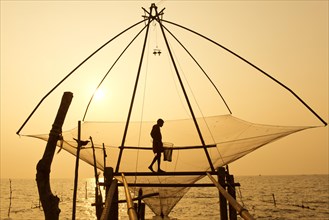 Fisherman holding a landing net in a Chinese fishing net at sunrise