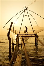 Fisherman holding a landing net in a Chinese fishing net at sunrise