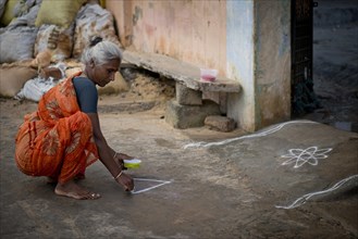 Elderly woman creating a traditional Rangoli