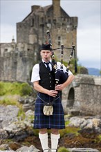 Bagpiper standing in front of Eilean Donan Castle