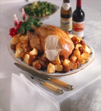 Whole roast turkey on a platter with roast potatoes
