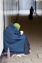 Homeless person wrapped in a blanket sitting in an underpass