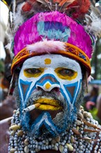 Man in a colourfully decorated costume with face paint and a cigarette at the traditional sing-sing gathering