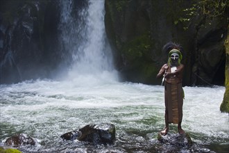 Decorated and painted tribal chief standing in front of a waterfall in the Highlands