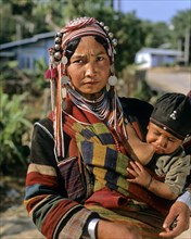 Woman from the people of the Akha wearing traditional costume while nursing a boy