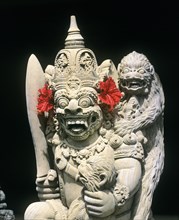 Demon's head carved out of stone decorated with red hibiscus flowers
