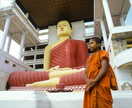 Monk standing in front of a giant Buddha statue in the Weherahena Temple