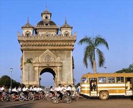 Bus and many cyclists passing Patou Xai triumphal arch