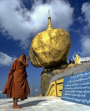 Buddhist Monk praying in front of the Golden Rock or Kyaiktiyo Pagoda