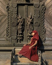 Monk sitting in front of a carved teak door