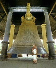Elderly woman with a wooden mallet standing in front of the largest intact bell in the world