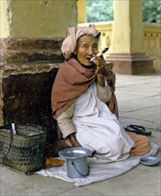 Elderly Burmese woman smoking a Cheerot cigar and wearing a headscarf