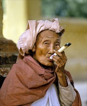 Elderly Burmese woman smoking a Cheerot cigar and wearing a headscarf