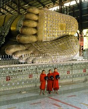 Monks holding begging bowls standing in front of the feet of the Reclining Buddha of Chauk Htat Gyi