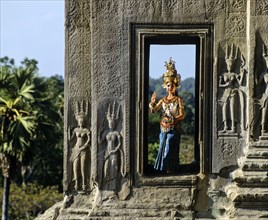 Temple dancer or apsara in a window of the temple of Angkor Wat beside apsara reliefs