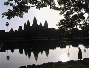 Main temple of Angkor Wat reflected in a pond with a monk standing at the shore