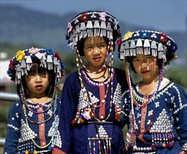 Three Lisu girls wearing colourful headdresses and the traditional costume of the mountain people
