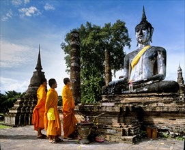 Three monks standing in front of the seated Buddha at Wat Mahathat
