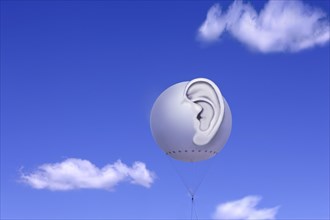 Tethered balloon with a three-dimensional human ear against a blue sky with white clouds