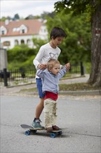 Older and younger brothers riding a skateboard