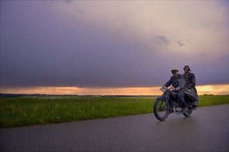 Two vintage motorcyclists in front of a dramatic cloudy sky