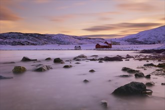 Red fishing hut before fjord in winter landscape