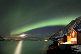 Red fishing huts on the fjord in winter with Northern Lights