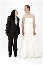 Bride wearing a suit and a groom wearing a wedding dress smiling at each other
