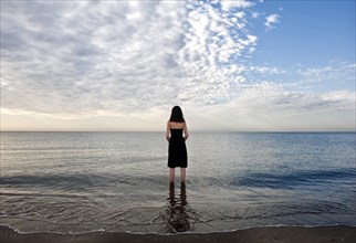 Woman wearing a black dress standing in the water of the sea