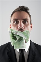 Man wearing a suit with 100 EUR banknotes stuffed in his mouth