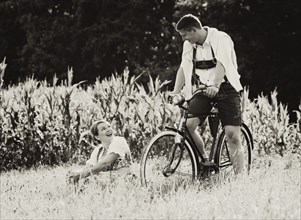 Man and a woman wearing traditional costume with an old bicycle within a natural landscape