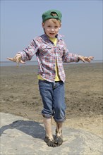 Boy with his hands and feet full of mud in the mudflats of the Wadden Sea