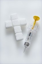 Sugar cubes in a cross-shape with a syringe filled with insulin