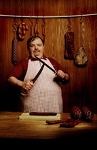 Fat butcher sharpening a filleting knife in a butcher's store with a wooden ambience