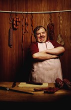 Fat butcher smiling with his arms crossed in a butcher's store with a wooden ambience