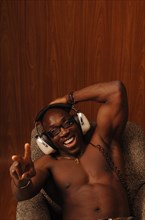 Young muscular bare-chested man sitting in an armchair with headphones