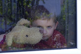 Boy looking out of a window with water drops