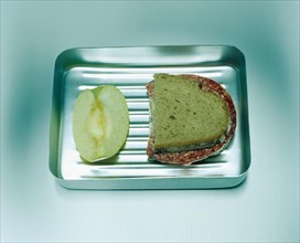 Salami bread and a piece of apple in an aluminium lunch box
