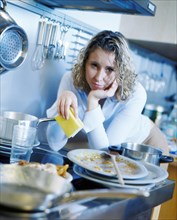 Annoyed woman holding a sponge while standing in a kitchen with dirty dishes