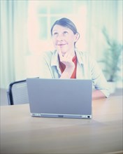 Woman sitting in front of a laptop and looking upwards