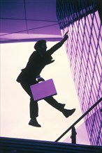 Man wearing a suit and holding a briefcase as a silhouette jumping with a hand held up in the air