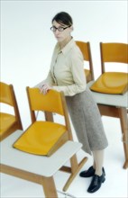 Strict female teacher standing at old school desks with orange chairs