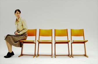 Woman sitting at the far corner intimidated with a number of old school orange chairs