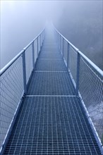 Steel bridge in the fog crossing over an Alpine stream