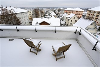 Two snow-covered chairs on a terrace