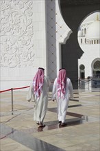 Two men in Arab dress walking in front of the Sheikh Zayed Mosque