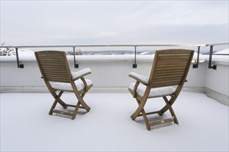 Two snow-covered chairs on a terrace