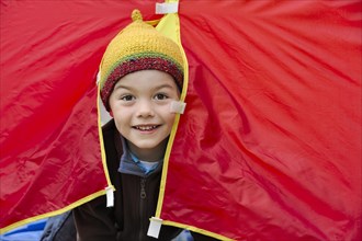 Boy with a knited cap looking out of a red tent