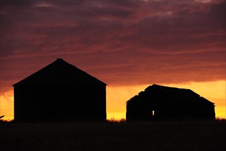 Wrecked barn with silo in silhouette at sunrise on the prairie