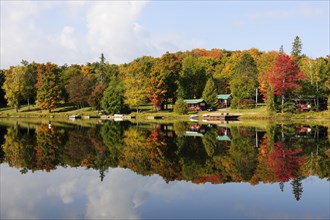 Forest in autumn colours and houses reflected in Galeairy Lake